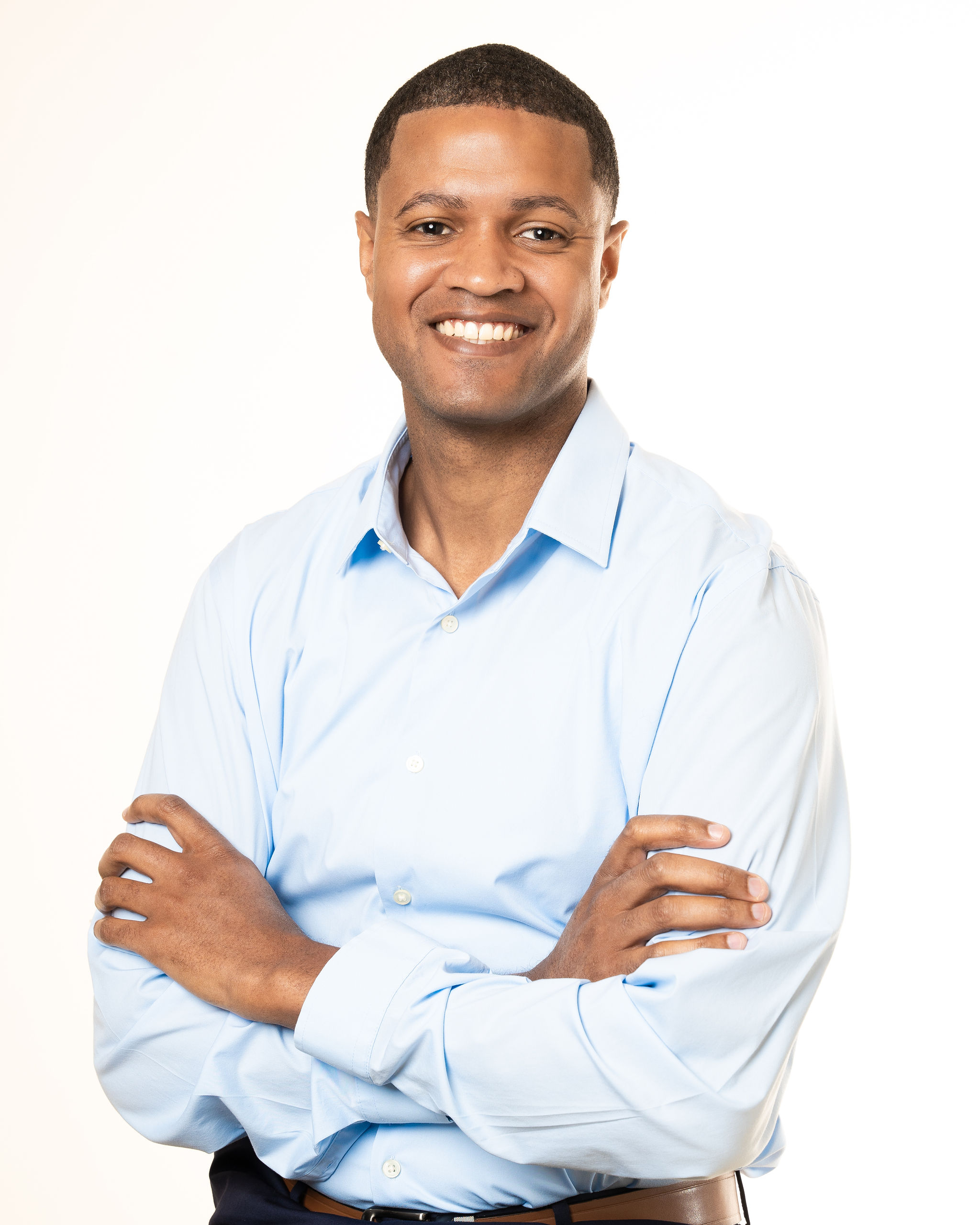 Portrait of Brian Wasson. Brian is a black man with short black hair. He is wearing a light blue shirt and smiling at the camera.